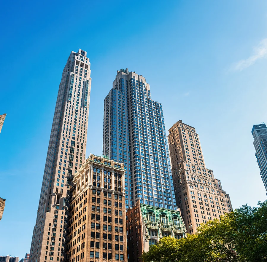 A New York cityscape featuring tall skyscrapers under a clear blue sky, with the tops of trees visible at the bottom - Out of Town patient resources in New York City